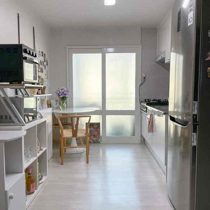 白とナチュラルカラーの縦長キッチン、丸いダイニングテーブルとキッチン家電が配置された雰囲気のあるインテリア