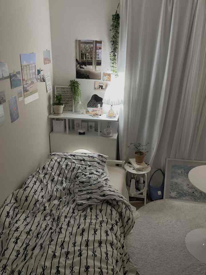 ホワイトトーンの寝室、リボン柄の寝具と植物が配置されたシンプルで落ち着いたインテリア