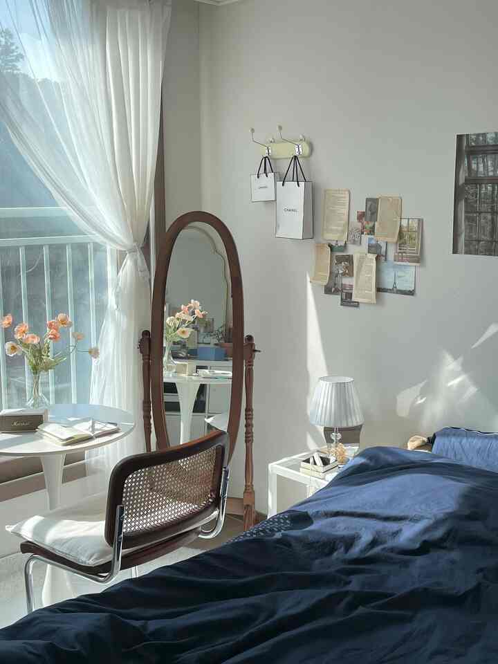 ネイビーの寝具がある寝室、窓際に全身鏡とカーテンが配置された落ち着いた空間