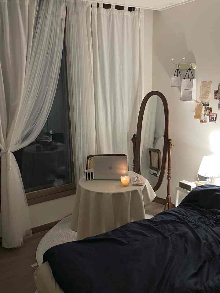 ナチュラルな色調の寝室、木製の全身鏡と白いカーテン、ダークブルーの掛け布団カバーが配置された落ち着いた雰囲気のインテリア