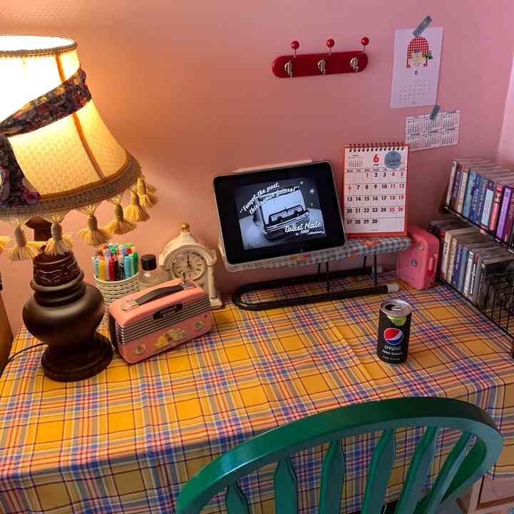 黄色のタータンチェックのテーブルクロスが敷かれたヴィンテージ風ホームオフィス、ピンクのレトロラジオとアイパッドが置かれた温かみのある作業空間