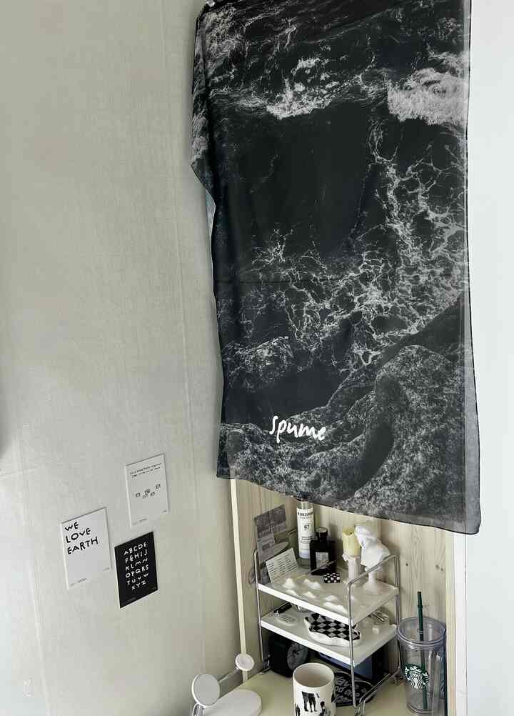 白い壁と黒のファブリックポスターが調和する狭い空間、本棚とヴィンテージオブジェが配置された雰囲気のあるインテリア