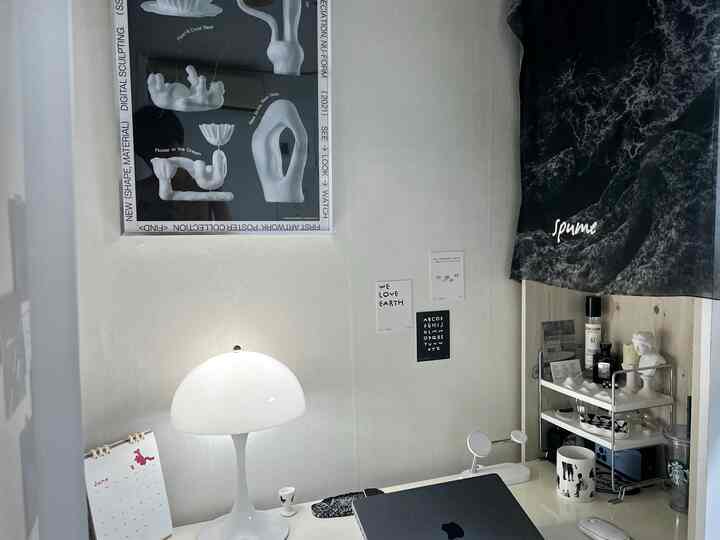 ホワイトトーンのミニマルモダンなホームオフィス、小さな棚の上にテーブルランプと石膏のオブジェが配置された清潔感のある作業空間