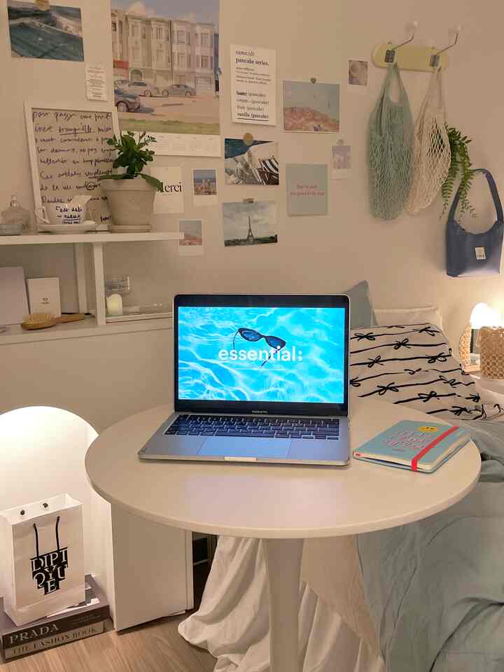 白とナチュラルカラーのワンルーム寝室、円形テーブルにノートパソコンと壁に飾られた額縁が配置された雰囲気のあるホームオフィス空間