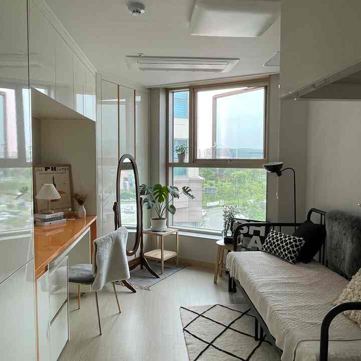 ナチュラルカラーと木目調が際立つ6坪の寝室、窓際に大型の全身鏡と植物が配置された印象的な空間