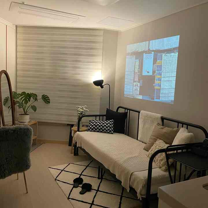 ベージュとホワイトの色調のリビングルーム、デイベッドとフロアランプ、全身鏡が配置された雰囲気のあるホームシネマ空間