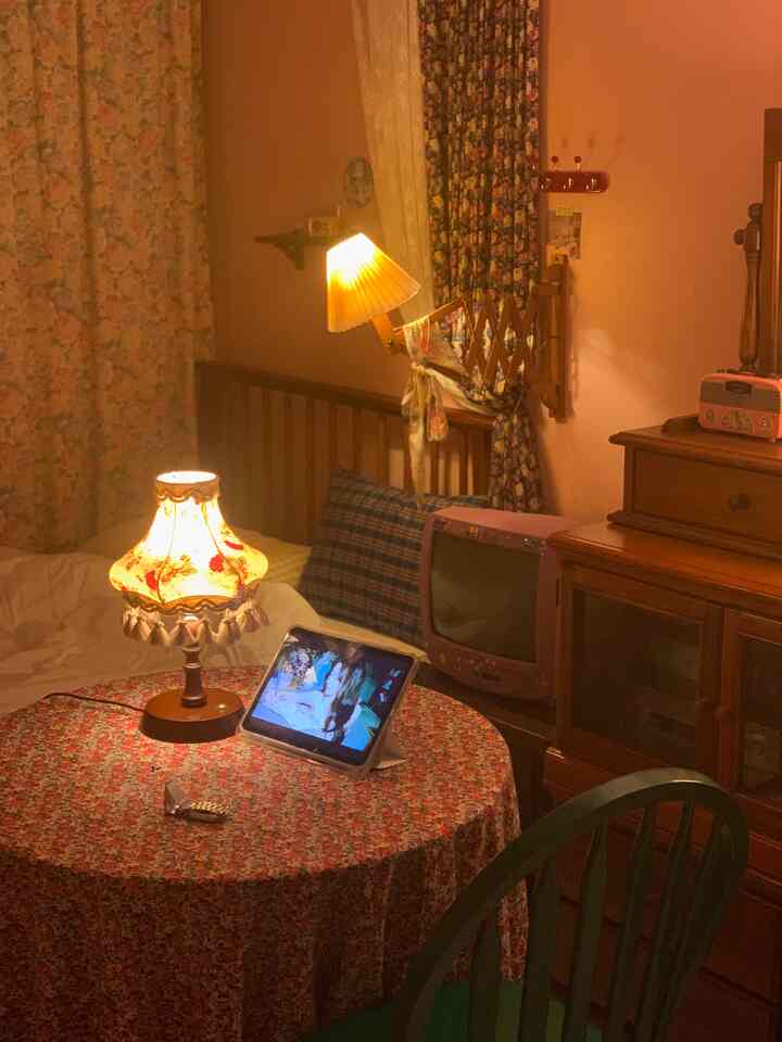 温かみのある木目調と花柄のカーテンが調和する寝室。丸テーブルとアンティーク照明が居心地の良い雰囲気を演出。