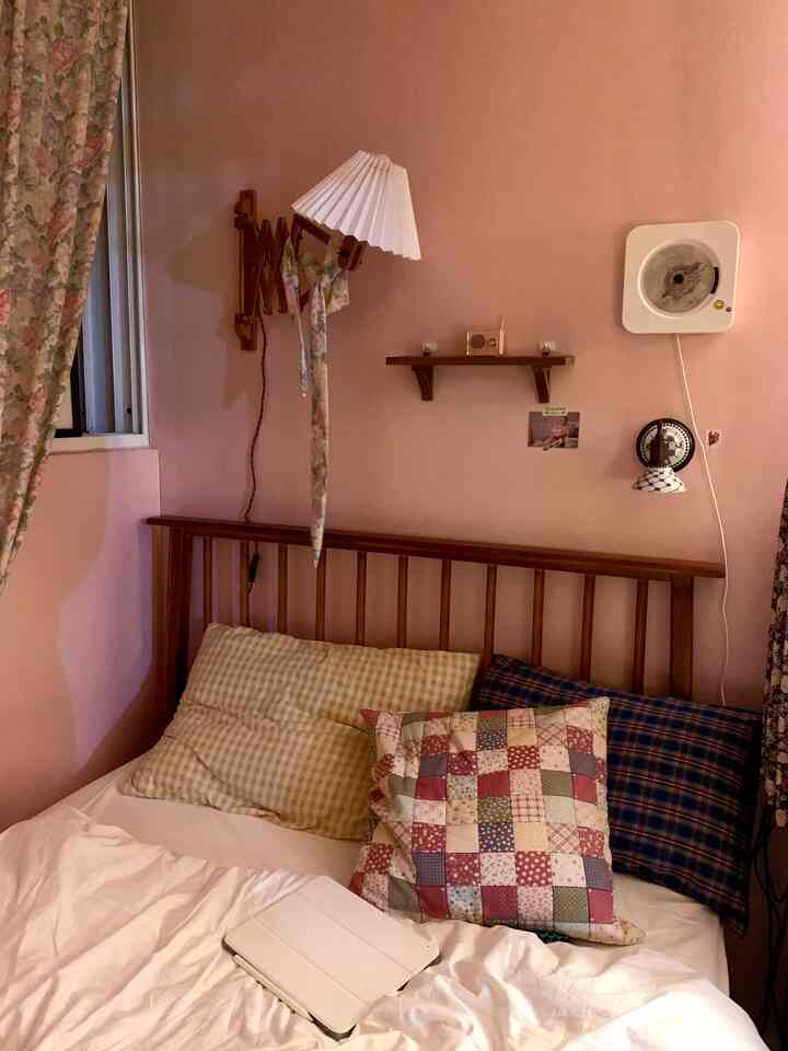 ピンク色の壁と木目調のベッドフレーム、白い寝具が配置された落ち着いた雰囲気の寝室