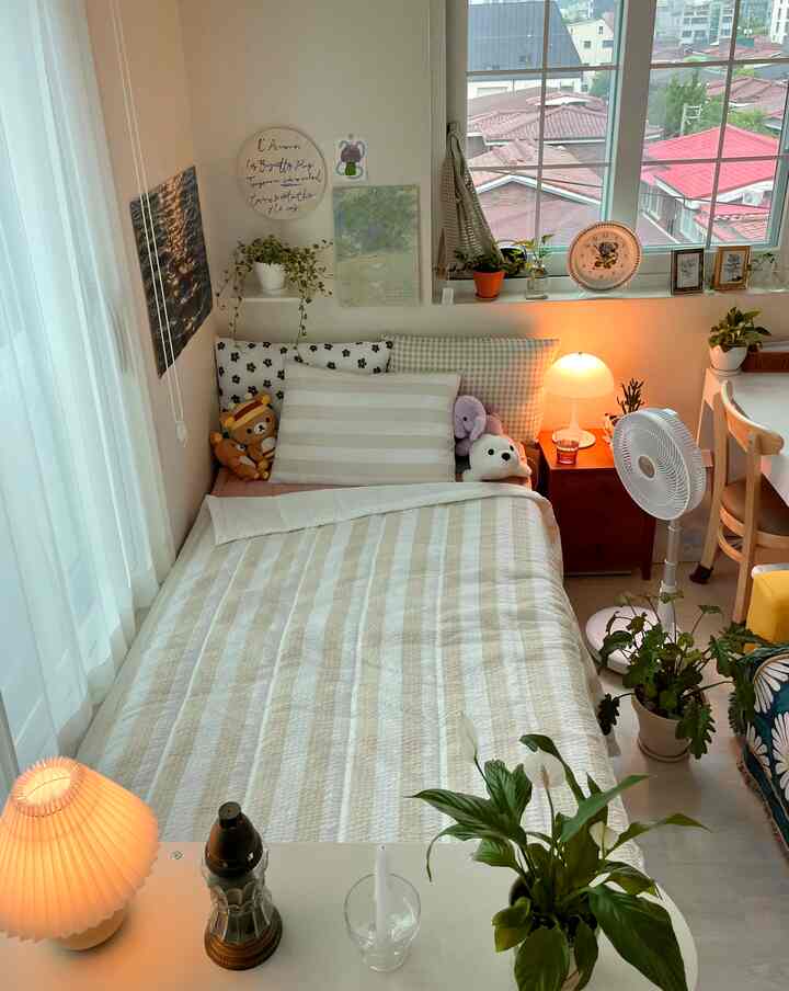 白とベージュの色調の寝室、窓辺に植物と照明が配置された落ち着いたコンパクトな空間