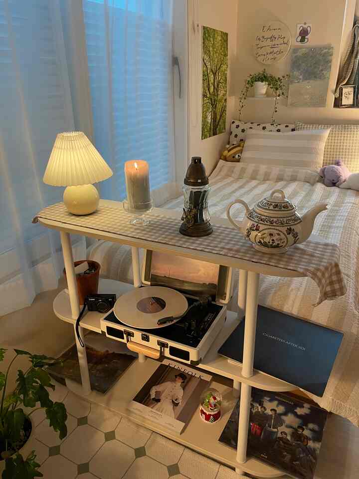 ホワイトとベージュの色調の寝室、3段棚に照明やキャンドル、ターンテーブル、雑誌が配置された落ち着いた空間