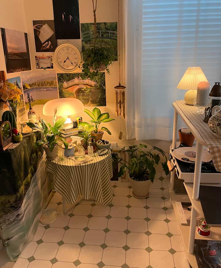 ナチュラルな色調の狭い部屋、多数の植物とテーブルランプが配置された雰囲気のある空間