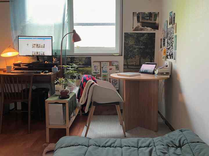 自然なライトブラウンとグリーンの色調の小さなホームオフィス、木製デスクとアームチェア、植物が配置された落ち着いた雰囲気のインテリア