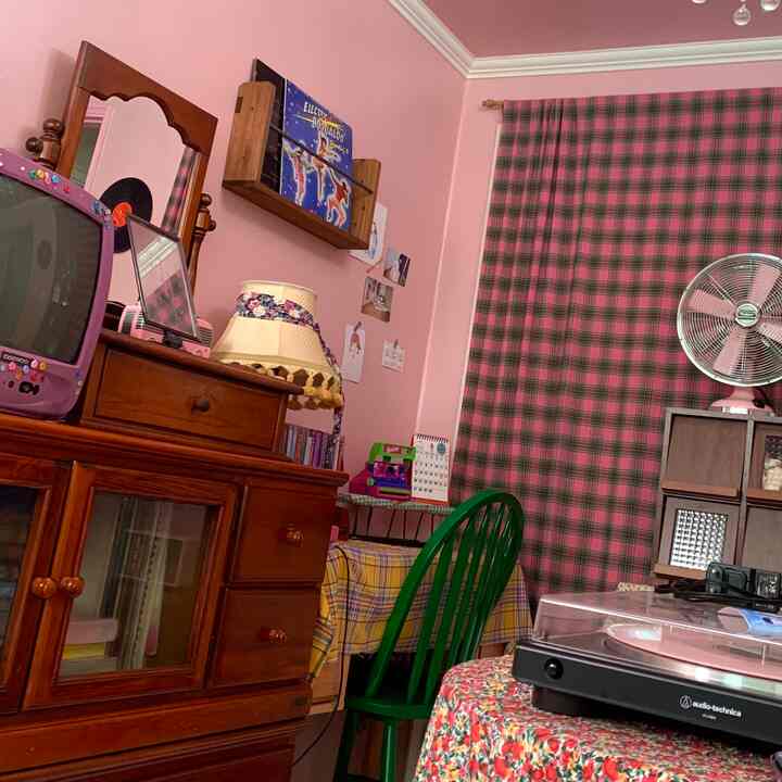 ピンクの壁とチェック柄のカーテン、木製家具とヴィンテージ雑貨が配されたレトロな雰囲気の空間