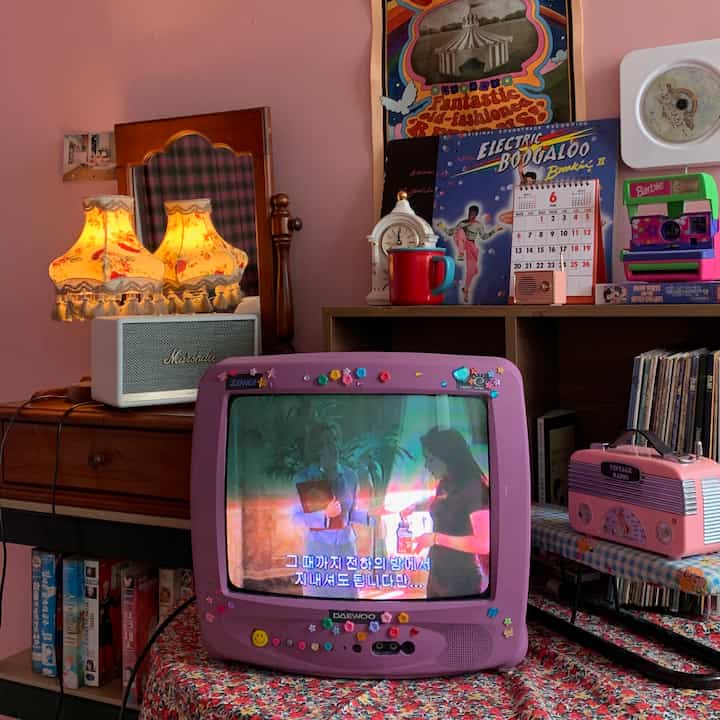 ピンク色の壁とヴィンテージテレビ、多彩な小物が配置されたレトロなリビング