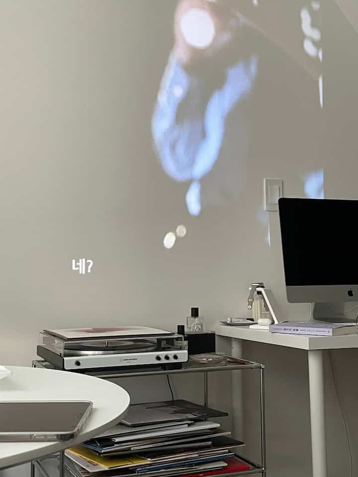 明るいホワイトトーンの一人暮らし用ホームオフィス、デスクトップとレコードプレーヤーが配置されたモダンなインテリア