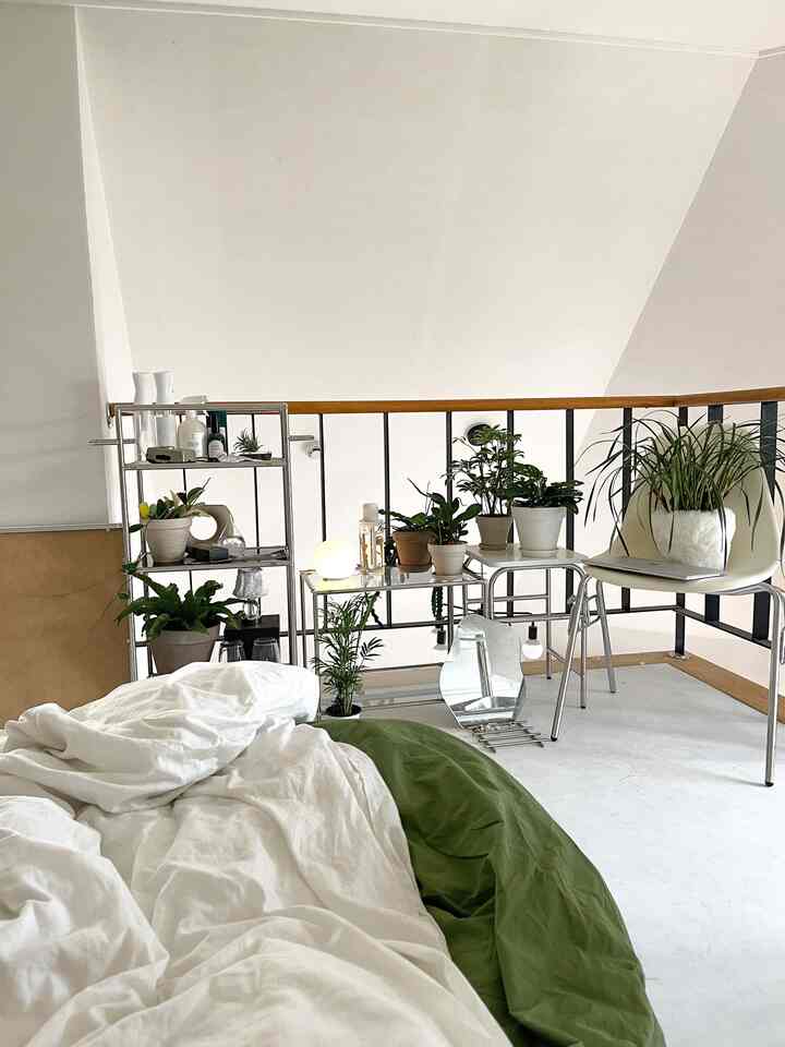 ナチュラルな色調の寝室、白い寝具と複数の植物がナイトテーブルや棚に配置された雰囲気のあるインテリア