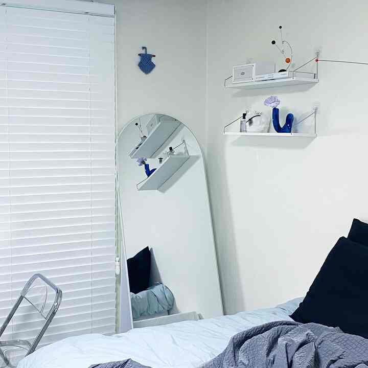 白とネイビーカラーの寝室、アーチ型全身鏡と透明椅子、壁棚の花瓶が配置された清潔でナチュラルモダンな雰囲気のあるインテリア
