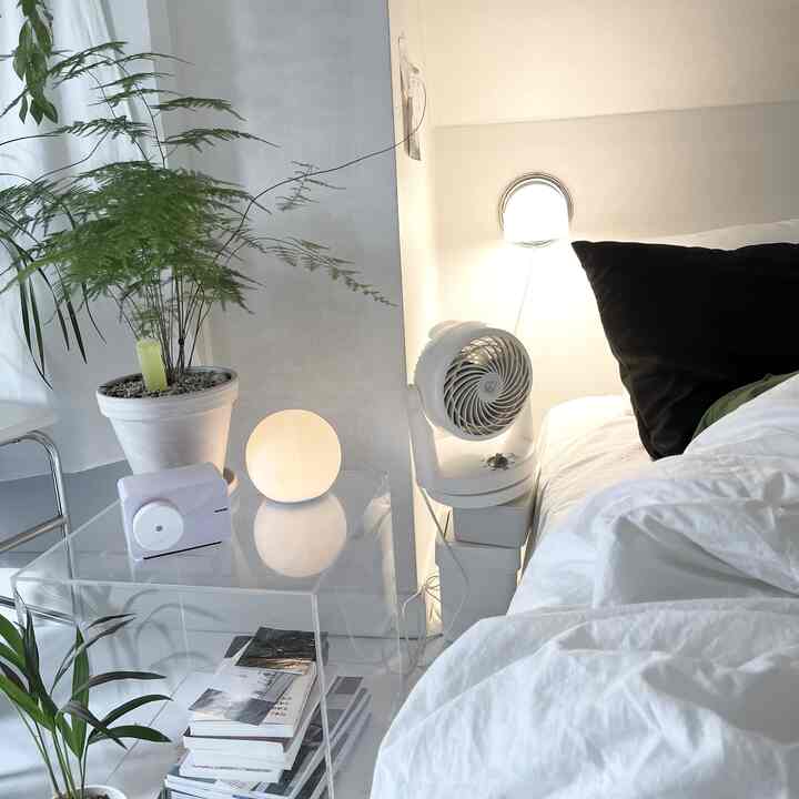 ホワイトトーンの寝室、透明なアクリルナイトテーブルとムードライト、植物が調和した落ち着いたインテリア