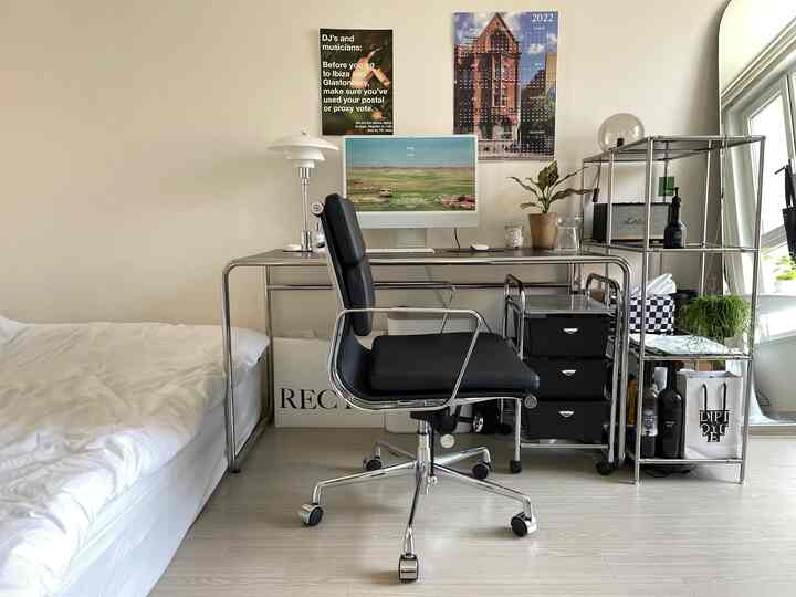 ナチュラルトーンのワンルーム、ホワイトのベッドとクロームのミッドセンチュリーモダンなホームオフィス、観葉植物が配置された落ち着いた雰囲気のインテリア