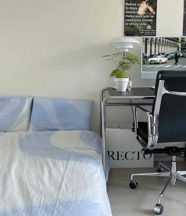 白い壁とスカイブルーの模様寝具がある寝室、モダンなデスクと黒のオフィスチェアが配置された清潔な空間