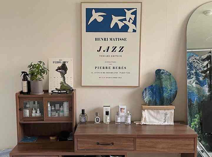 アイボリーの壁とブラウンの木目調家具が配置された空間、ポスターと曲線的な鏡が調和する雰囲気のあるインテリア