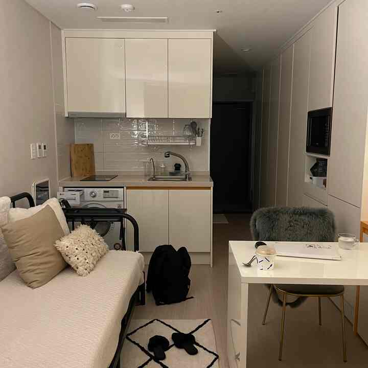 白と黒のトーンのワンルーム、ビルトインクローゼットと金属製ベッドフレーム、デスクが配置されたモダンでコンパクトなインテリア