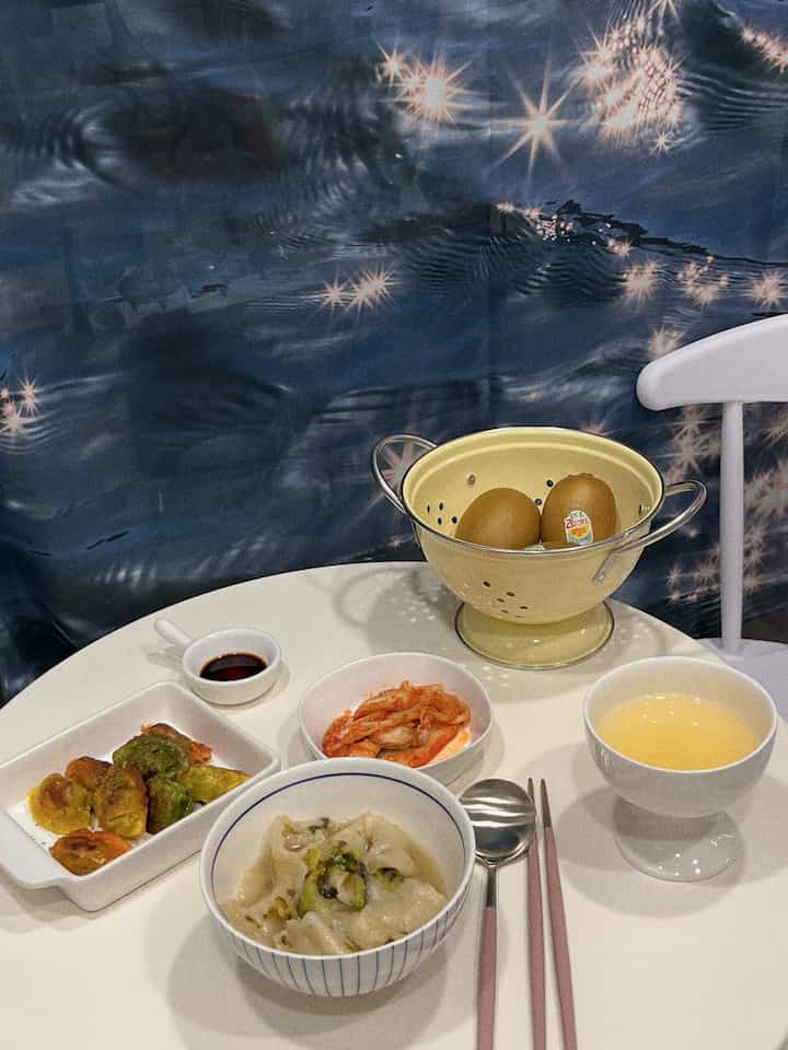 青い背景と白いダイニングテーブル、黄色いコランダーがあるシンプルな食事空間