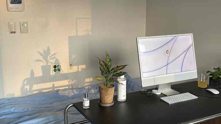 柔らかなホワイトとブルーの色調の寝室兼ホームオフィス、黒いデスクにiMacと植物が置かれた落ち着いた清潔感のあるインテリア