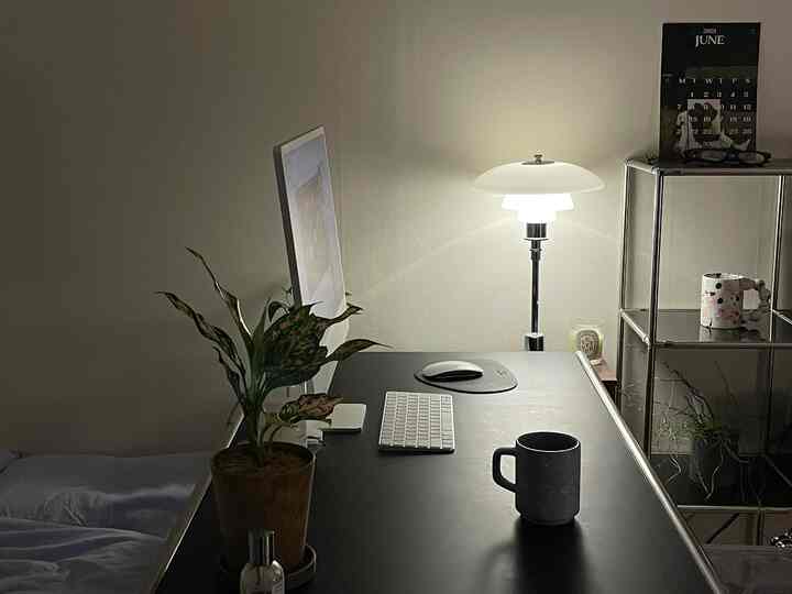 黒いデスクと白い壁があるモダンな寝室のホームオフィス空間、デスクの上に植物とテーブルランプが配置された落ち着いた雰囲気のインテリア