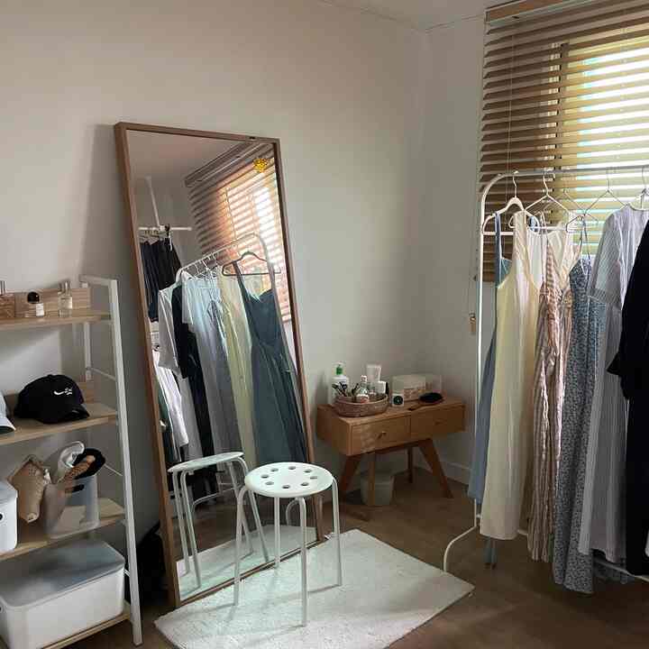 ウッドトーンとホワイトが調和したウォークインクローゼット、大きな全身鏡とハンガーラック、化粧台が配置された雰囲気のあるインテリア