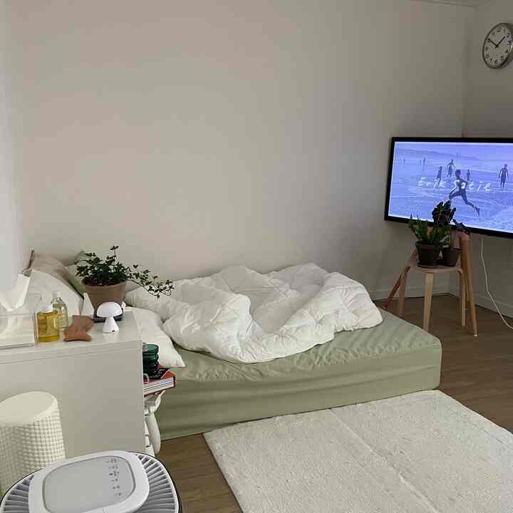 白と木目調が調和する寝室、クイーンサイズベッドとイーゼルタイプのテレビスタンド、スツールが配置された雰囲気のあるインテリア