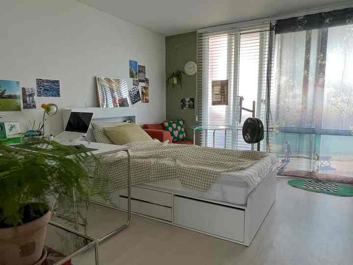 ホワイトとグリーンの調和が美しい4坪の寝室、ベッドとデスク、オレンジのソファが配置された落ち着いたコンパクトな空間