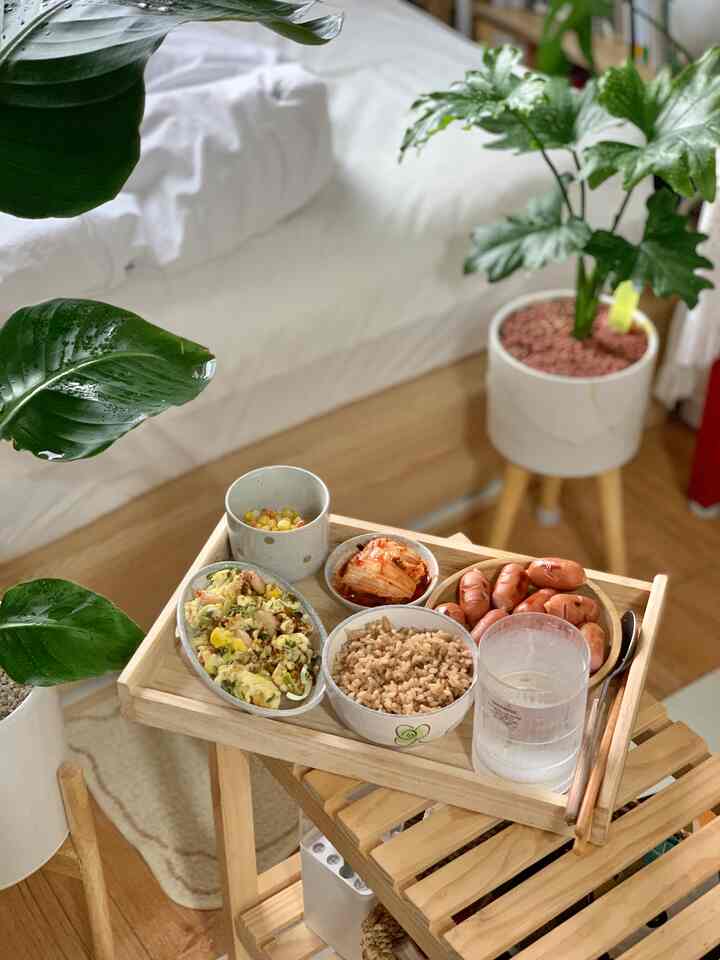 ナチュラルな木目調の寝室、ベッド脇の小さな棚に木製トレイと食事セットが置かれた雰囲気のあるインテリア