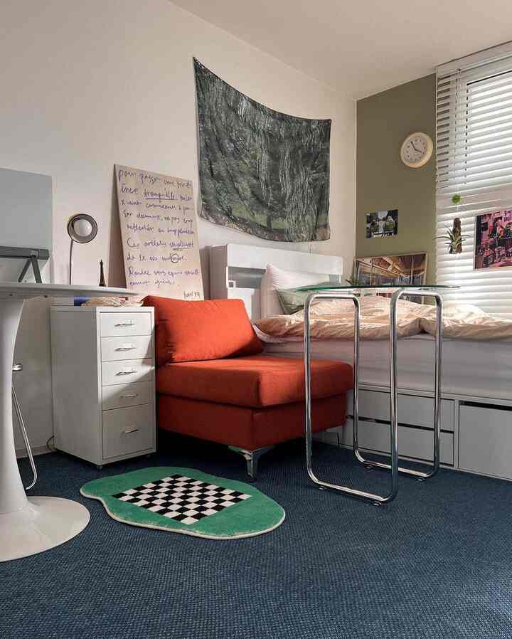 ブルーのカーペットとオレンジのソファが置かれた一人暮らしの寝室、シンプルでコンパクトな空間