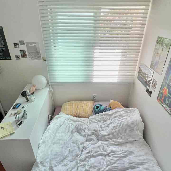 ホワイトトーンの寝室、窓にはホワイトのブラインドがあり、ベッドの横にドレッサーが配置された落ち着いた雰囲気のインテリア