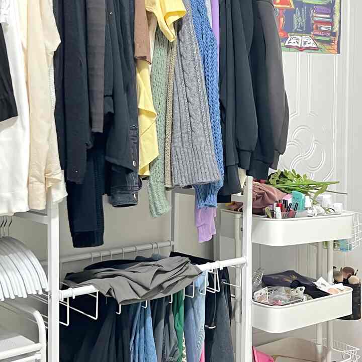 白を基調としたウォークインクローゼット、ハンガー付きの洋服ラックと収納用の白いトロリーが配置された整った収納空間