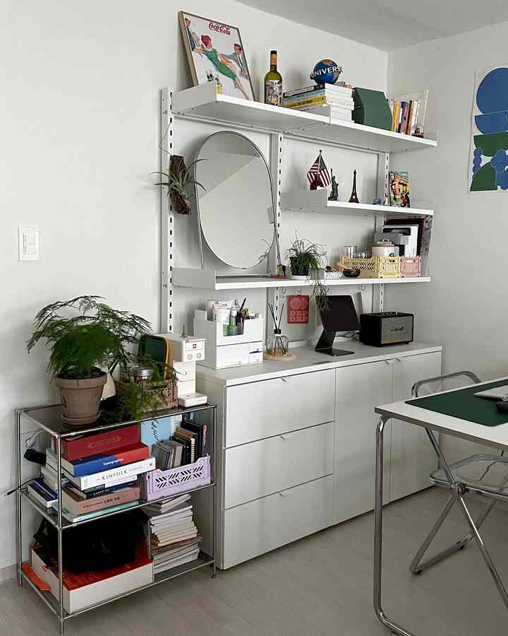 白を基調としたコンパクトなホームオフィス、壁掛け棚や収納家具、植物が配置された清潔感のあるインテリア