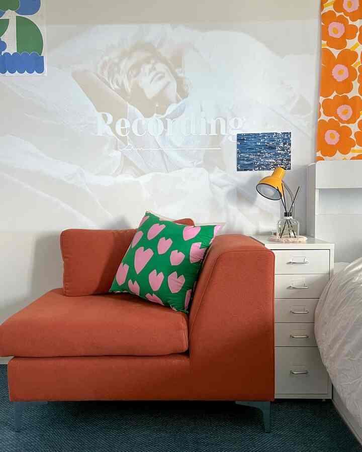 温かみのあるオレンジ色と白い背景のリビングルーム、オレンジのソファとハート柄クッション、黄色い壁の照明が調和した居心地の良いインテリア