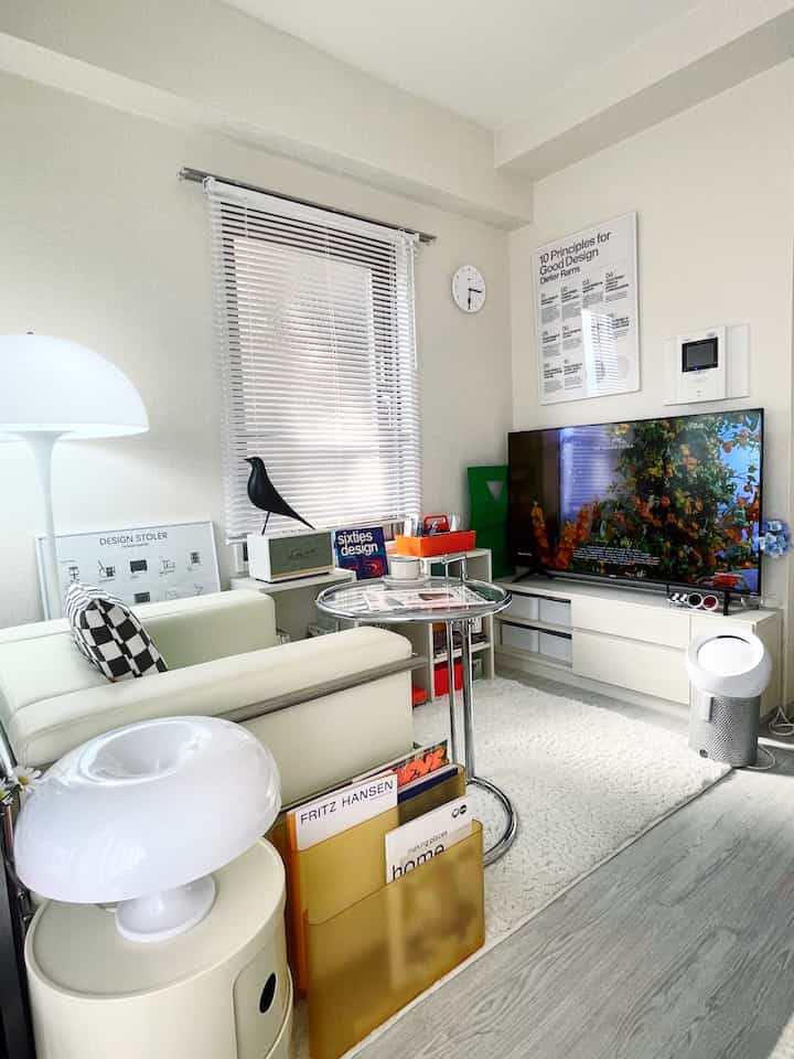 ホワイトトーンのワンルームリビング、クローム製のC型テーブルとミッドセンチュリーモダンの装飾が配置された、清潔で居心地の良いインテリア