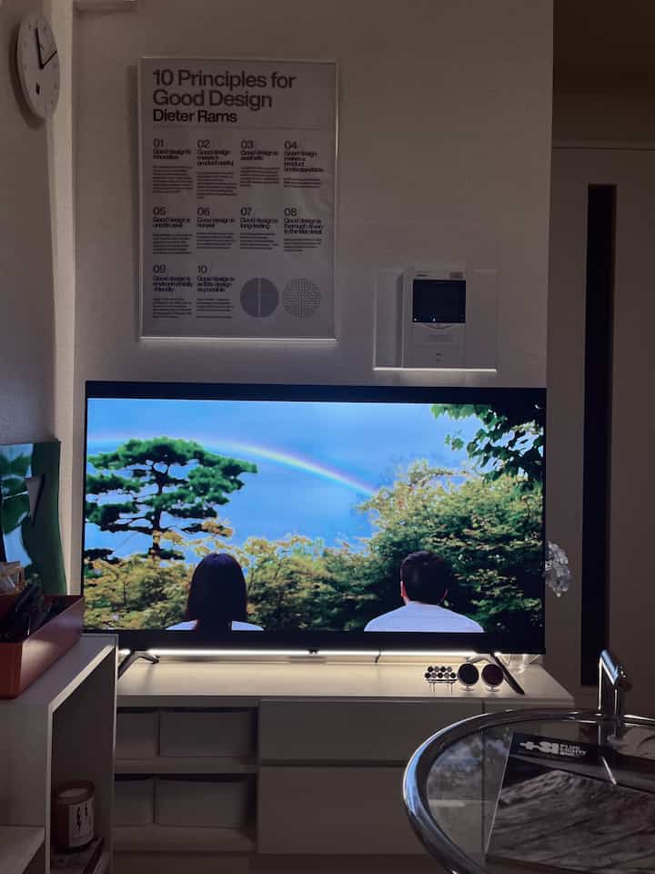 白を基調としたワンルームのリビング、LEDバックライトとミッドセンチュリーモダンのポスターが配置された印象的な空間