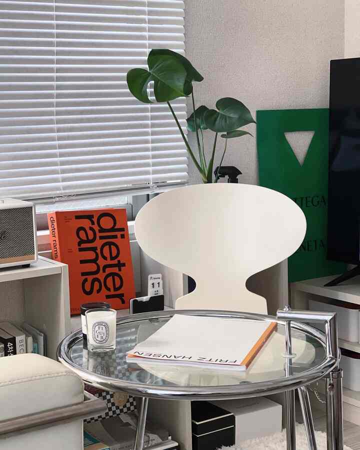 白と緑のトーンのリビング、ヴィンテージのアントチェアと大きな植物、キャンドルが置かれたガラスのサイドテーブルがある落ち着いたインテリア