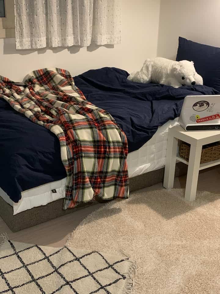 白とネイビーのトーンの寝室、ベッドとチェック柄の毛布が配置されたアットホームでシンプルな空間