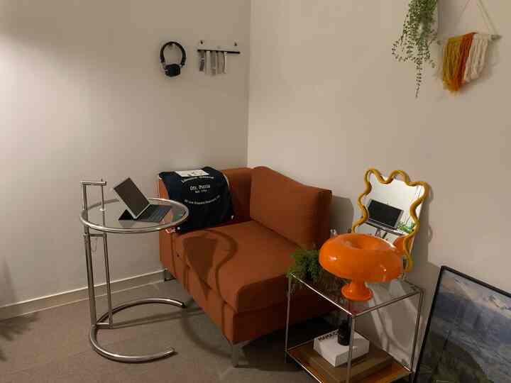 ナチュラルカラーのコンパクトなリビングルーム、焼けたオレンジ色のソファとガラストップのサイドテーブルが配置されたミッドセンチュリーモダンの印象的な空間