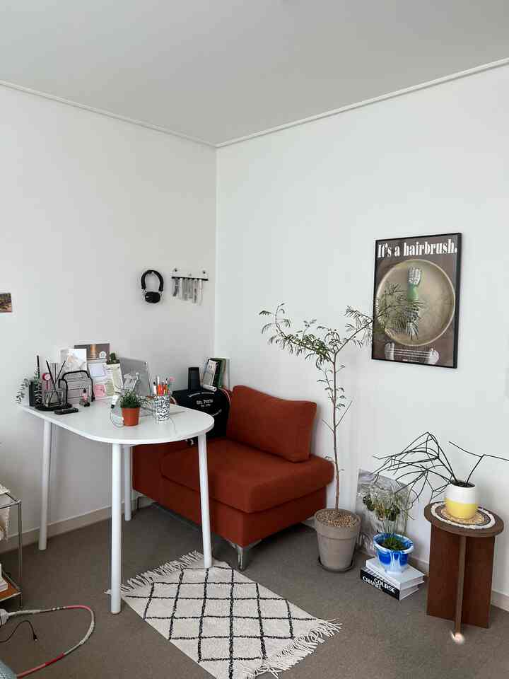 白い壁と天井のモダンなリビング兼ホームオフィス、オレンジのアームチェアと白いデスクが配置された落ち着いたシンプルな空間