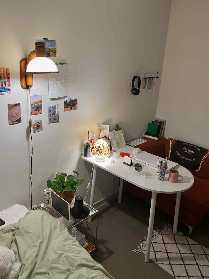 白い壁と茶色のソファがあるコンパクトなホームオフィス兼一人暮らしの部屋、机の上に照明と植物が配置された居心地の良い空間