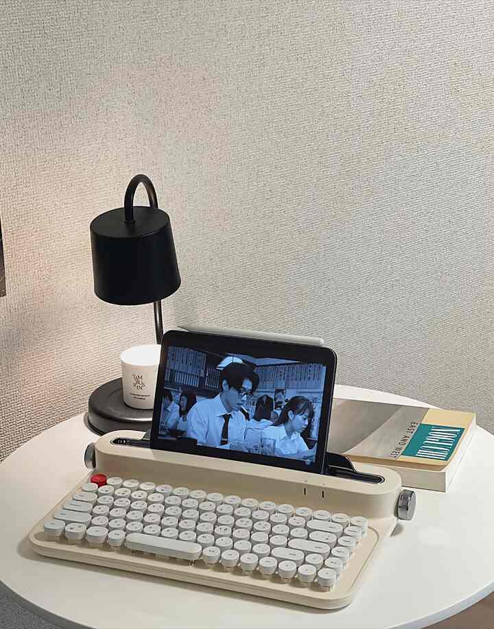 白い丸いダイニングテーブルにレトロスタイルのキーボードとタブレット、黒いテーブルランプが配置された落ち着いたホームオフィス空間