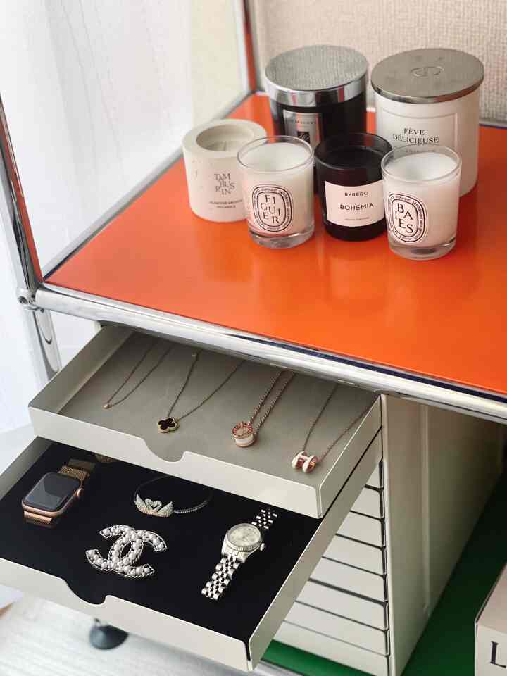 鮮やかなオレンジの棚にキャンドルが複数置かれ、下部の白い引き出しにはアクセサリーが美しく整理されたシンプルでモダンな空間