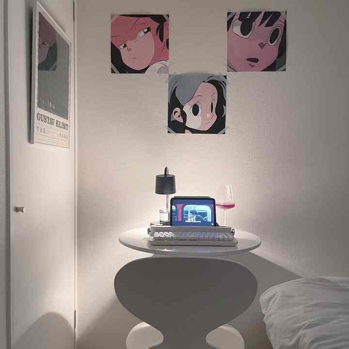 白を基調とした狭い部屋、丸テーブルと椅子、アニメポスターが配置されたミニマルなホームオフィス空間