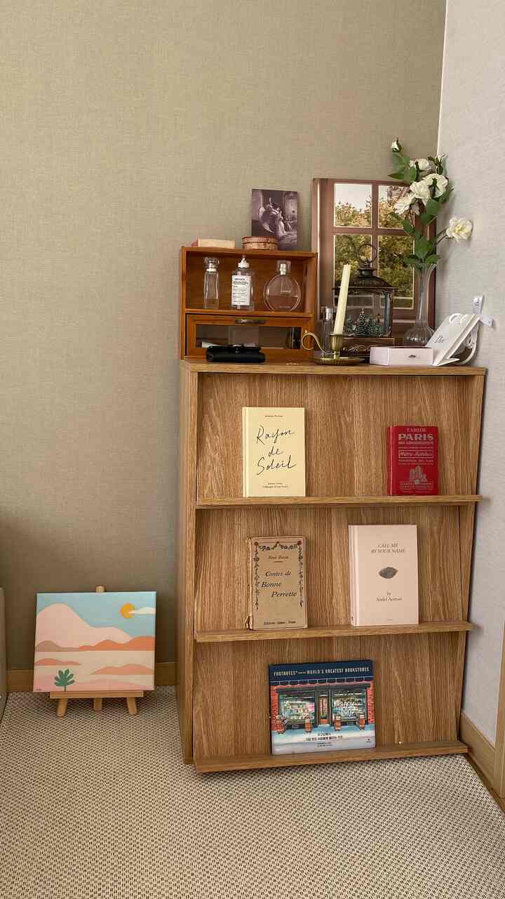 ベージュの壁と木目調の本棚がある小さなウォークインクローゼット、本とインテリア小物が配置された雰囲気のある空間