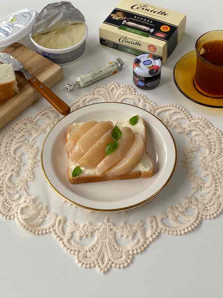 白とゴールドのトーンのホームカフェテーブル、桃のコンポートトーストが置かれた上品な皿とお茶がある雰囲気のある空間